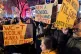 Demonstrators hold signs, one reading, at left, reading 