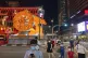 Pedestrians cross a street with a lit giant ox display to we
