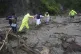 A woman is helped across a highway blocked by a landslide tr